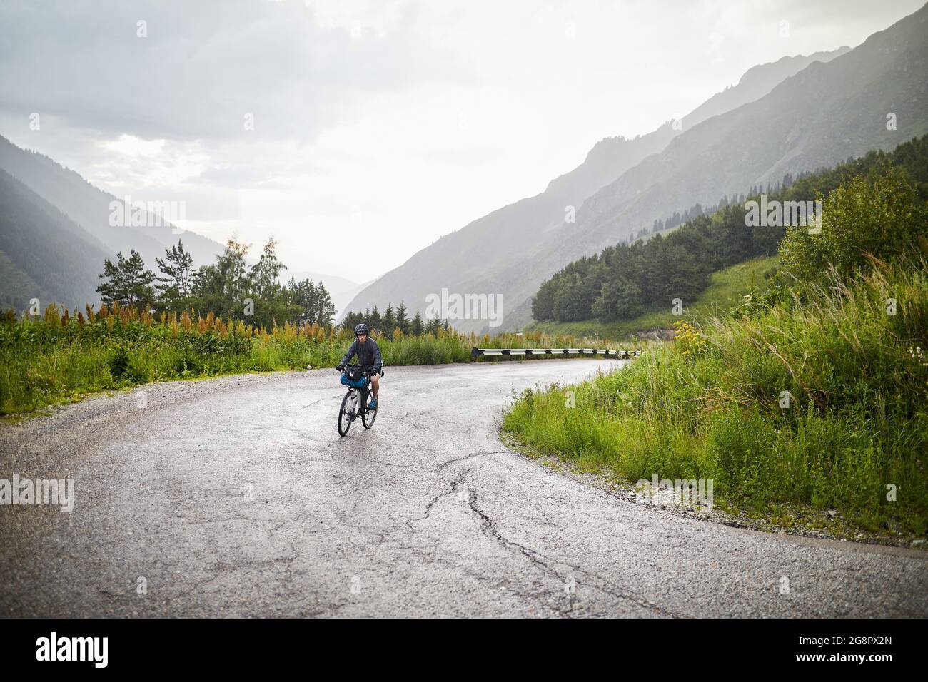 Uomo in bicicletta sulla strada di montagna serpentina al cielo piovoso sovrastato Foto Stock