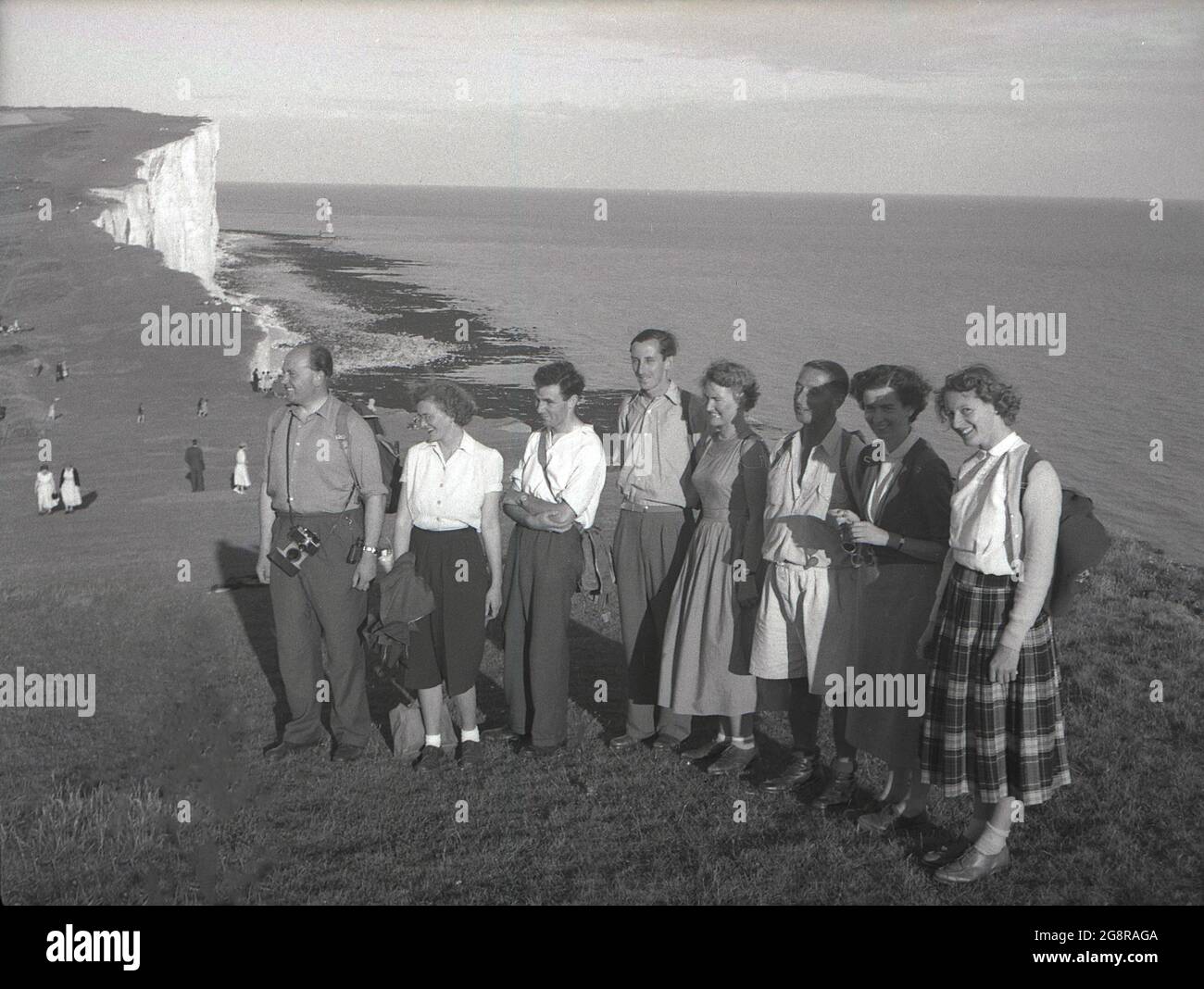 Anni '50, storico, un gruppo di adulti camminatori in abiti dell'epoca, fuori a sud giù a Beachy Head, vicino a Eastbourne, East Sussex, Inghilterra, Regno Unito. La più alta scogliera di mare di gesso in Gran Bretagna, l'area circostante è famosa per i suoi sentieri per passeggiate, con magnifiche viste sul canale Inglese. Il faro offshore, costruito nel 1902 - e l'ultimo in Gran Bretagna - si può vedere nella baia in lontananza. Foto Stock