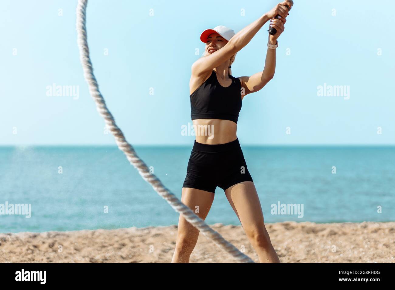 Bella giovane donna sportiva, l'atleta muove le corde in moto d'onda come parte dell'allenamento per bruciare il grasso, l'allenamento sulla spiaggia della città, Sport Foto Stock