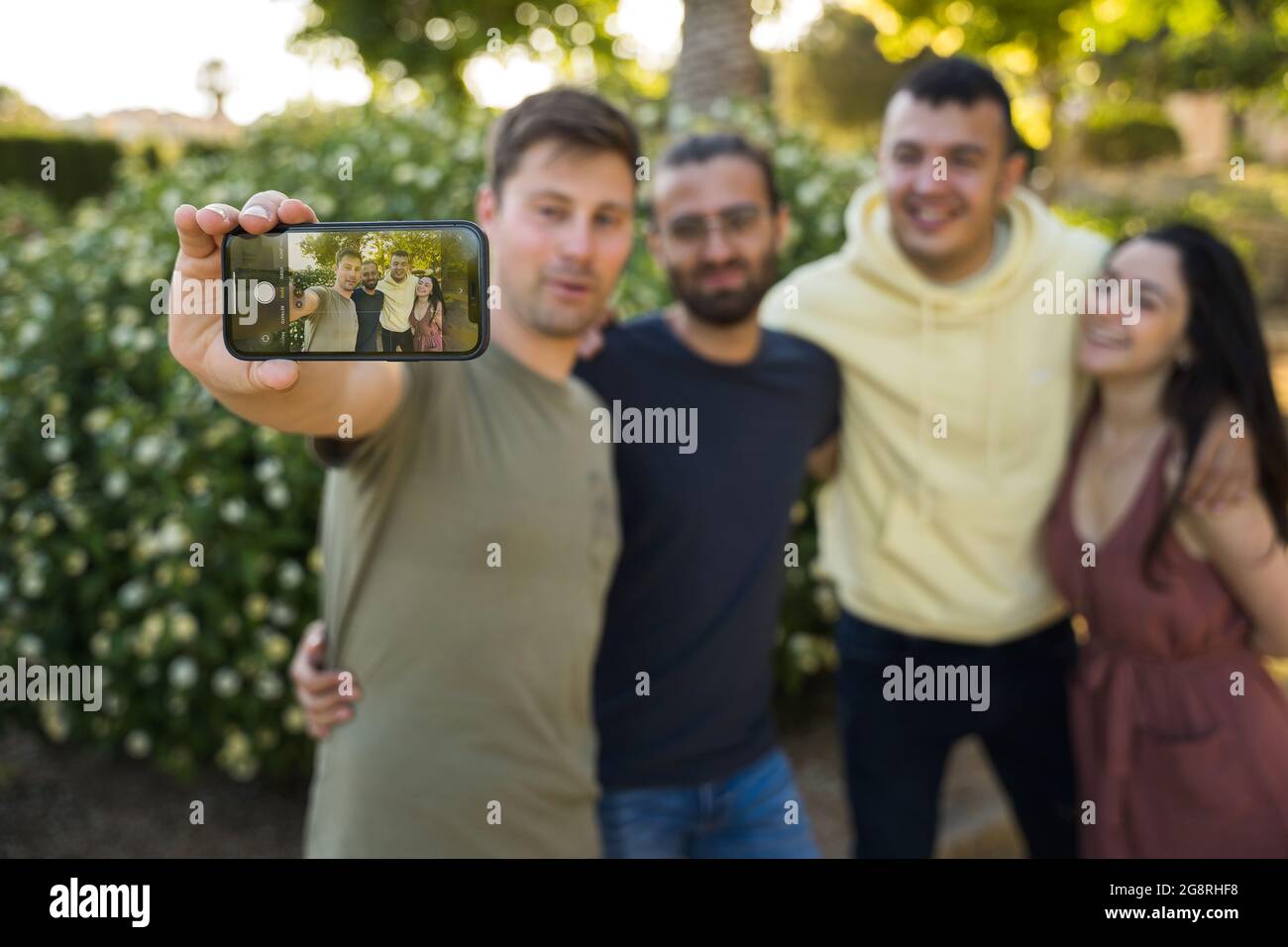 Amici che prendono un selfie insieme nel parco. Caucasici in abiti colorati. Sono felici di scattare una foto. L'attenzione è rivolta al telefono cellulare. Javea, Foto Stock