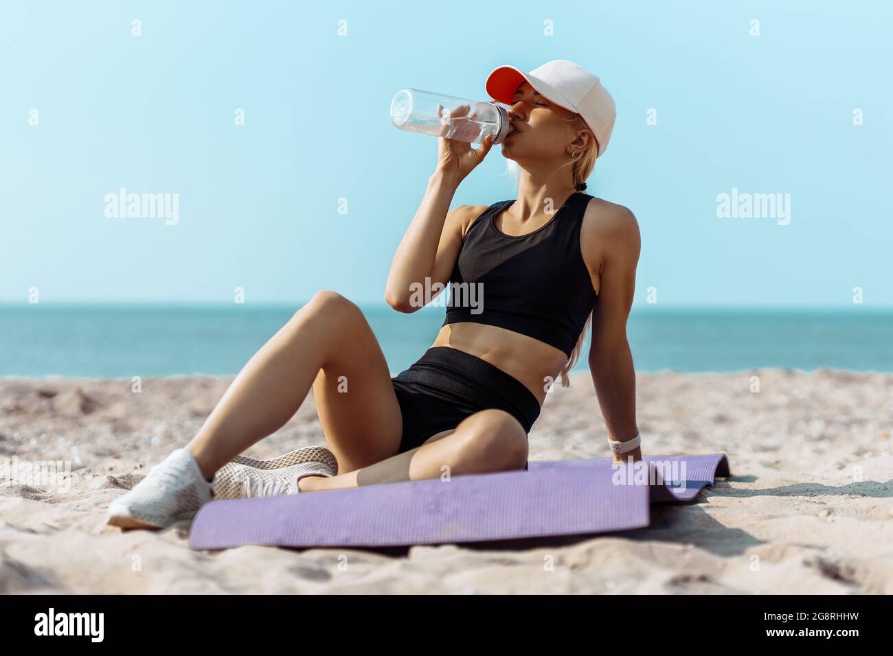 Fitness giovane donna in abbigliamento sportivo seduta e riposante dopo l'allenamento, all'aperto in spiaggia dopo l'allenamento mattutino, riposo e acqua potabile, Fitness Foto Stock