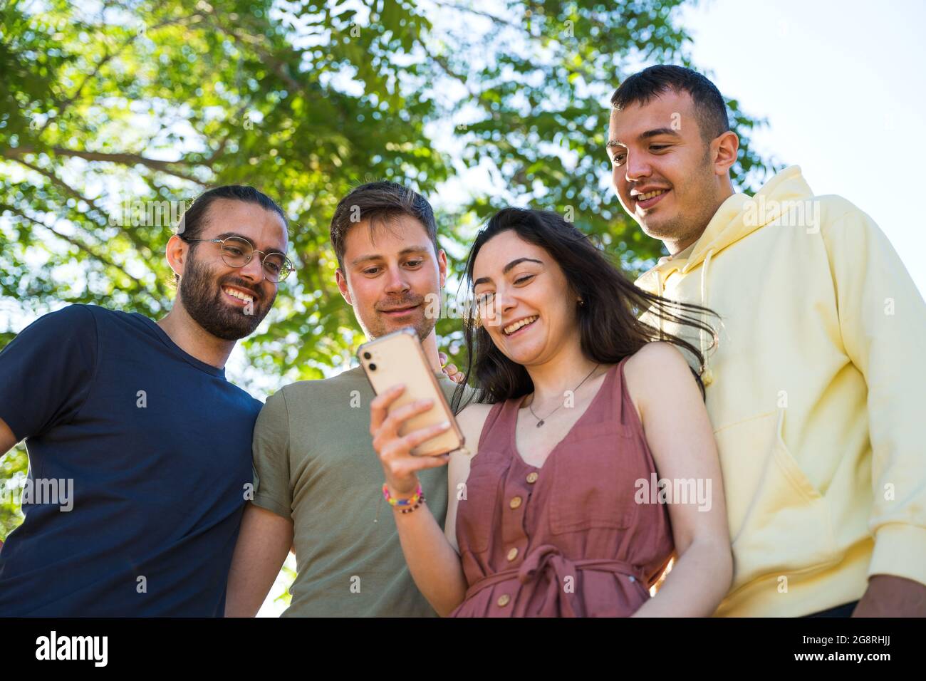 Gli amici sorridono mentre guardano un telefono cellulare. Sono insieme guardando lo stesso telefono mobile.They stanno indossando vestiti colorati. In un parco con Foto Stock