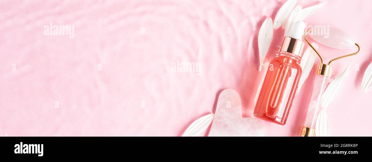 Bellezza cosmetica olio siero prodotto acido bottiglia e quarzo rullo viso guasha su sfondo rosa in acqua con margherita rosa. Cura naturale della pelle Foto Stock