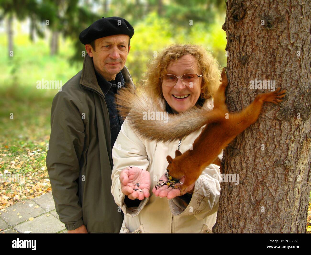 Felici e sorridenti gli anziani nutrono uno scoiattolo nel parco. Il concetto di ecologia, il rafforzamento delle relazioni familiari e l'escursionismo. Foto Stock