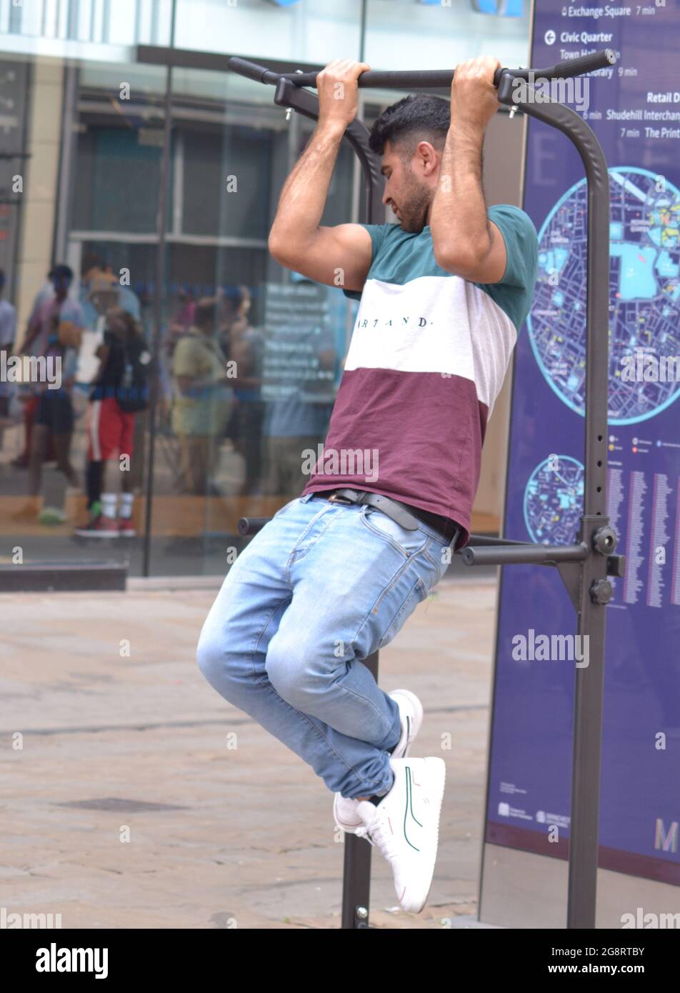 Gli uomini accettano una sfida per tenersi fuori terra per due minuti ad una stazione di pull-up e di immersione o tirare su rack per il fitness di gravità e l'addestramento del peso su Market Street, Manchester, Regno Unito. Nessuna foto riuscita. L'offerta era £5 se potevano farlo e l'offerta di un'audizione per un film come uomini forti. Foto Stock