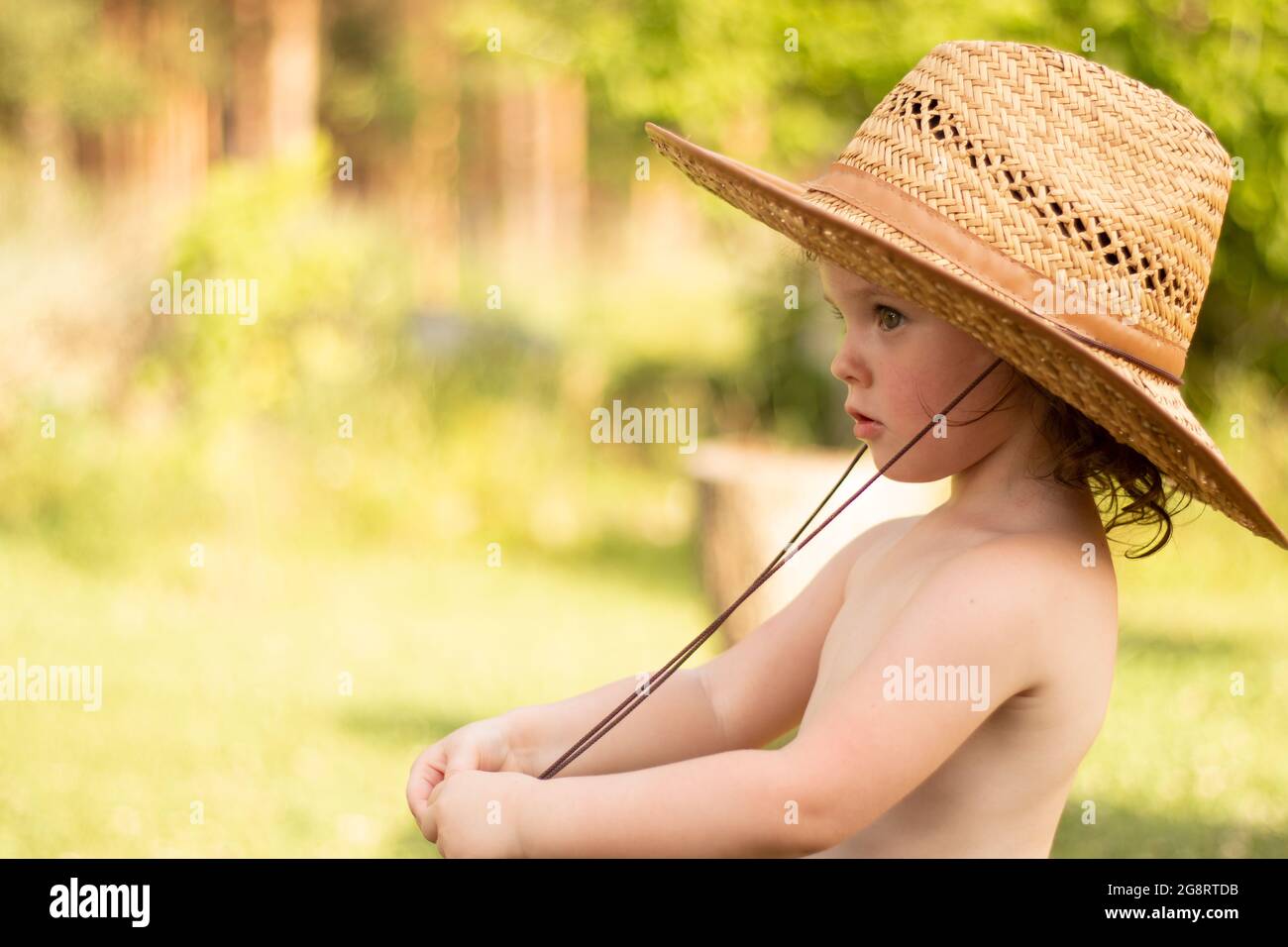 Un piccolo bambino carino messo a fuoco in un cappello di paglia tiene la sua corda del collo guardando in lontananza. Meravigliosi momenti d'infanzia nella vigna Foto Stock