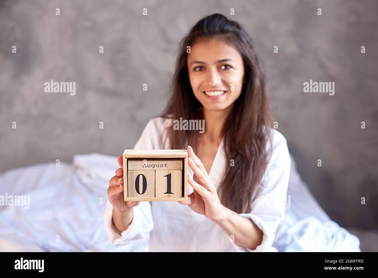 donna sorridente tenere in legno il calendario perpetuo nelle mani in camera da letto. Il 1° agosto è l'ultimo mese dell'estate Foto Stock