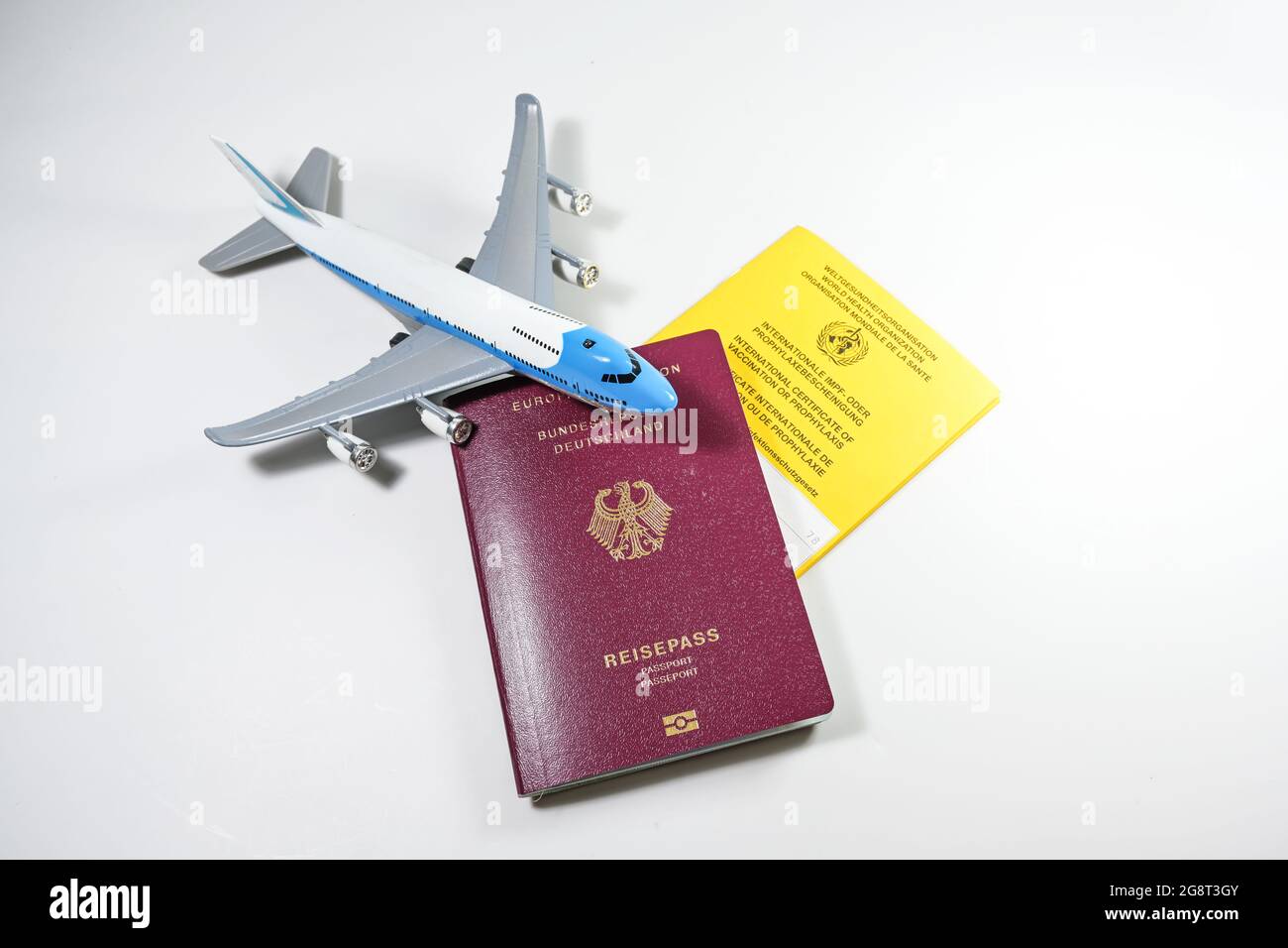 German Passport, libretto di certificati internazionali gialli di vaccinazione e un aeroplano giocattolo su sfondo grigio chiaro, concetto di requisiti di viaggio d Foto Stock