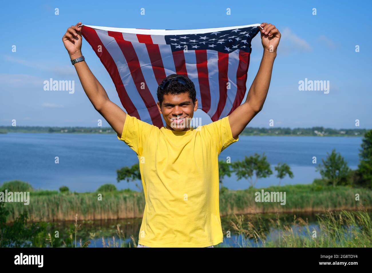Uomo che guarda la macchina fotografica e tiene orgogliosamente bandiera americana tra le sue braccia Foto Stock