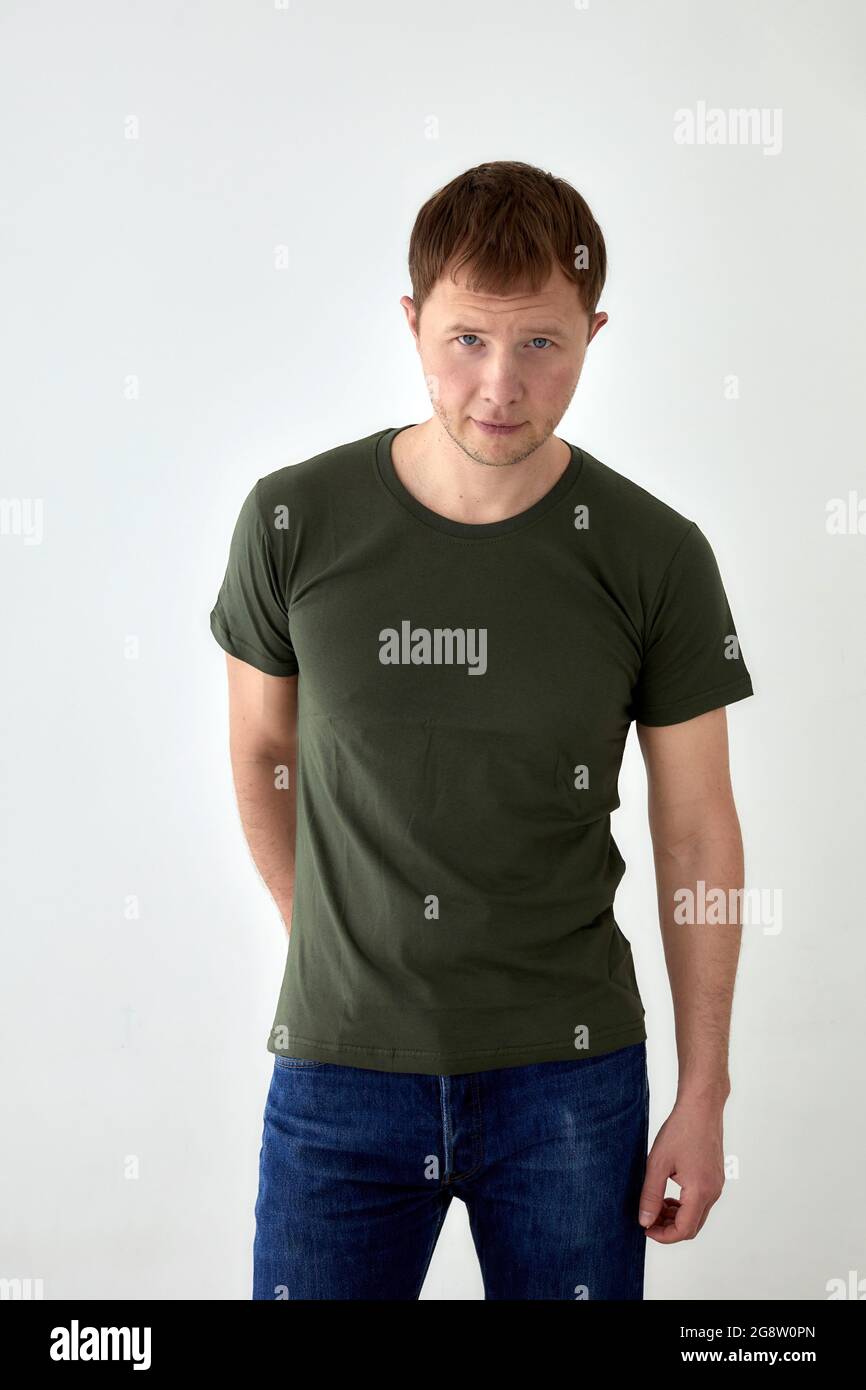 Bel giovane maschio in jeans con mano dietro e t-shirt verde scuro in piedi  su sfondo bianco e guardando la macchina fotografica Foto stock - Alamy