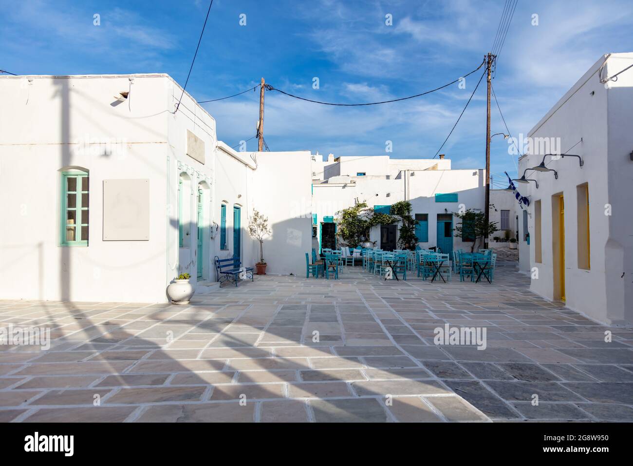 Isola di Serifos, Chora, Cicladi Grecia. Taverna tradizionale, vuota, dipinta di bianco, con tavoli in metallo, sedie in vimini blu, posti a sedere in una stree di ciottoli Foto Stock