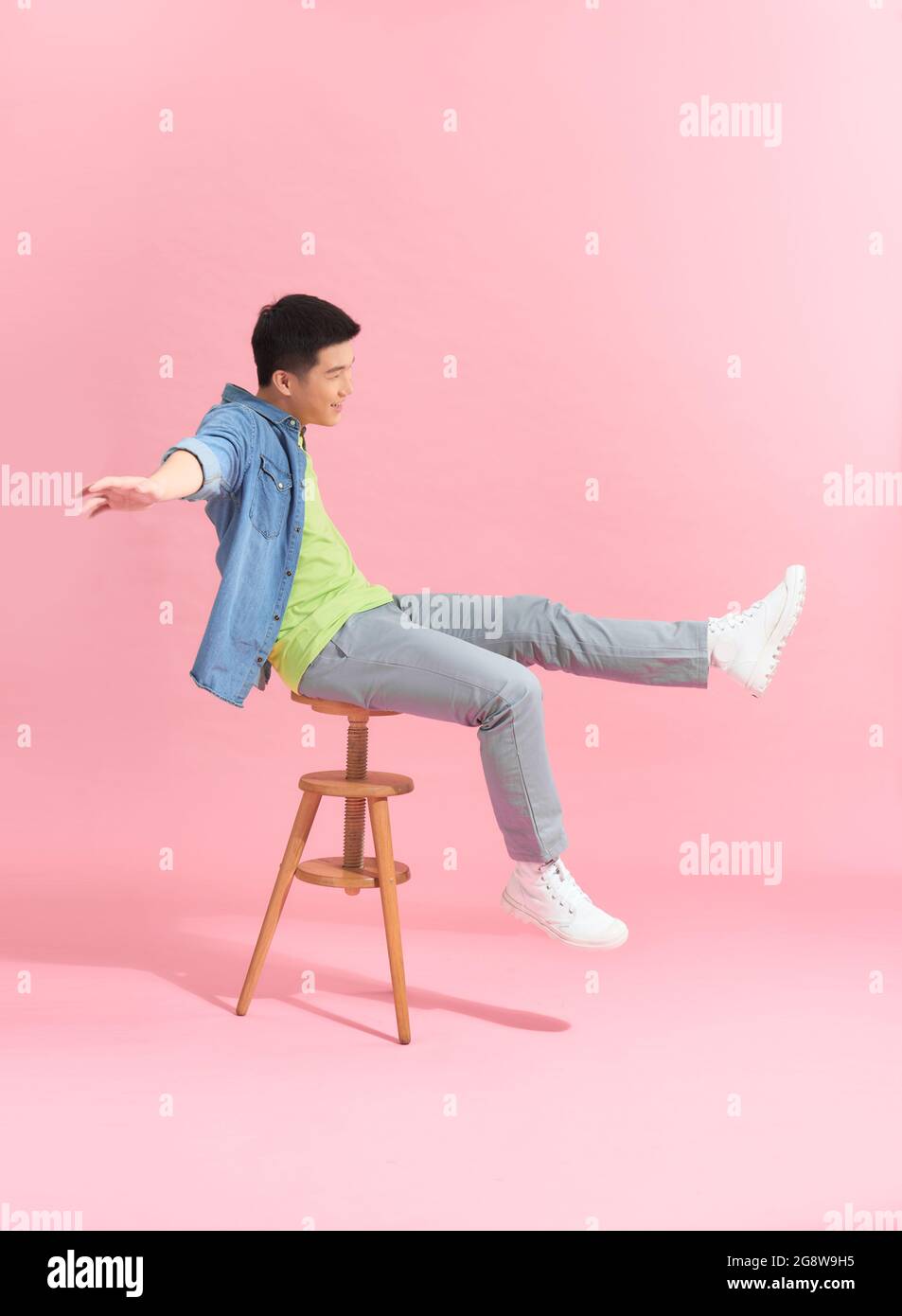 Un ragazzo contemplativo vestito seduto su uno sgabello su sfondo rosa nello studio Foto Stock