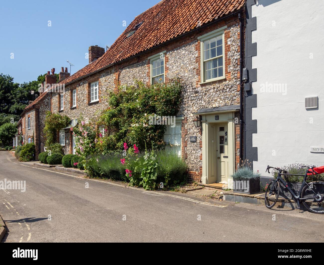Street scene in estate nel grazioso villaggio di Burnham Market, Norfolk, Regno Unito; fila di cottage selce che si affaccia sul verde. Foto Stock
