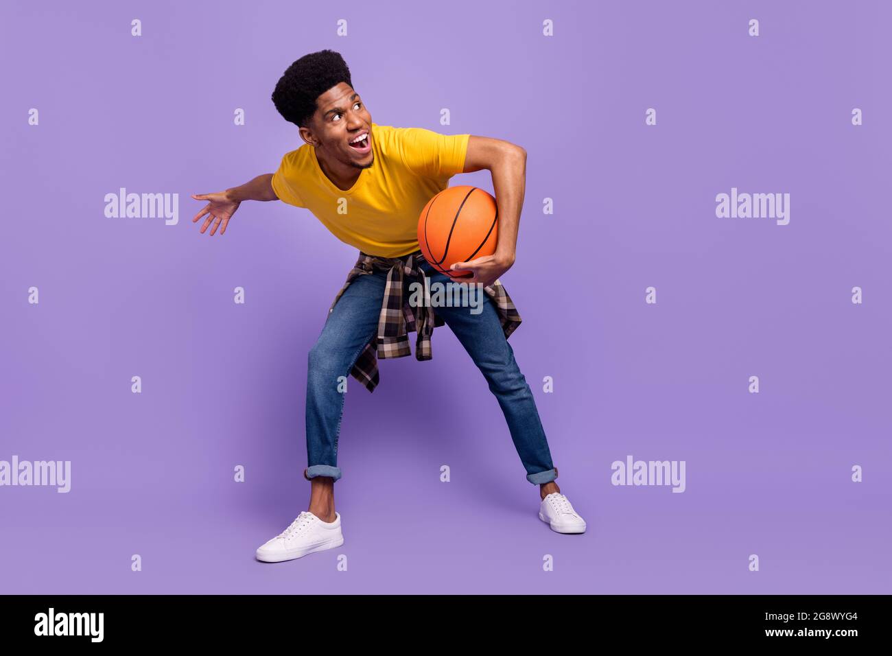 Vista di dimensioni del corpo di lunghezza intera di attraente ragazzo allegro che gioca a basket amatoriale avendo divertimento isolato su sfondo viola di colore viola Foto Stock