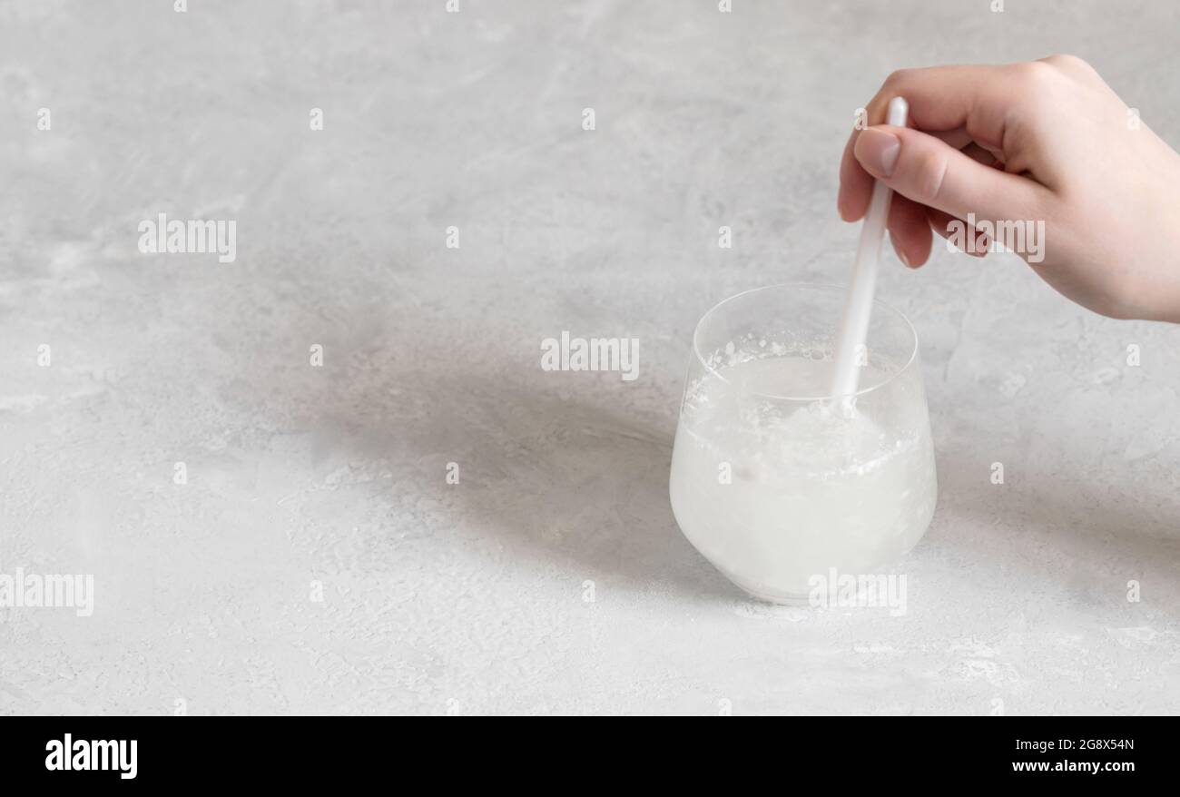 La mano mescola polvere di collagene o proteine in un bicchiere d'acqua su fondo grigio. Sano concetto di supplemento naturale. Spazio per il testo. Foto Stock