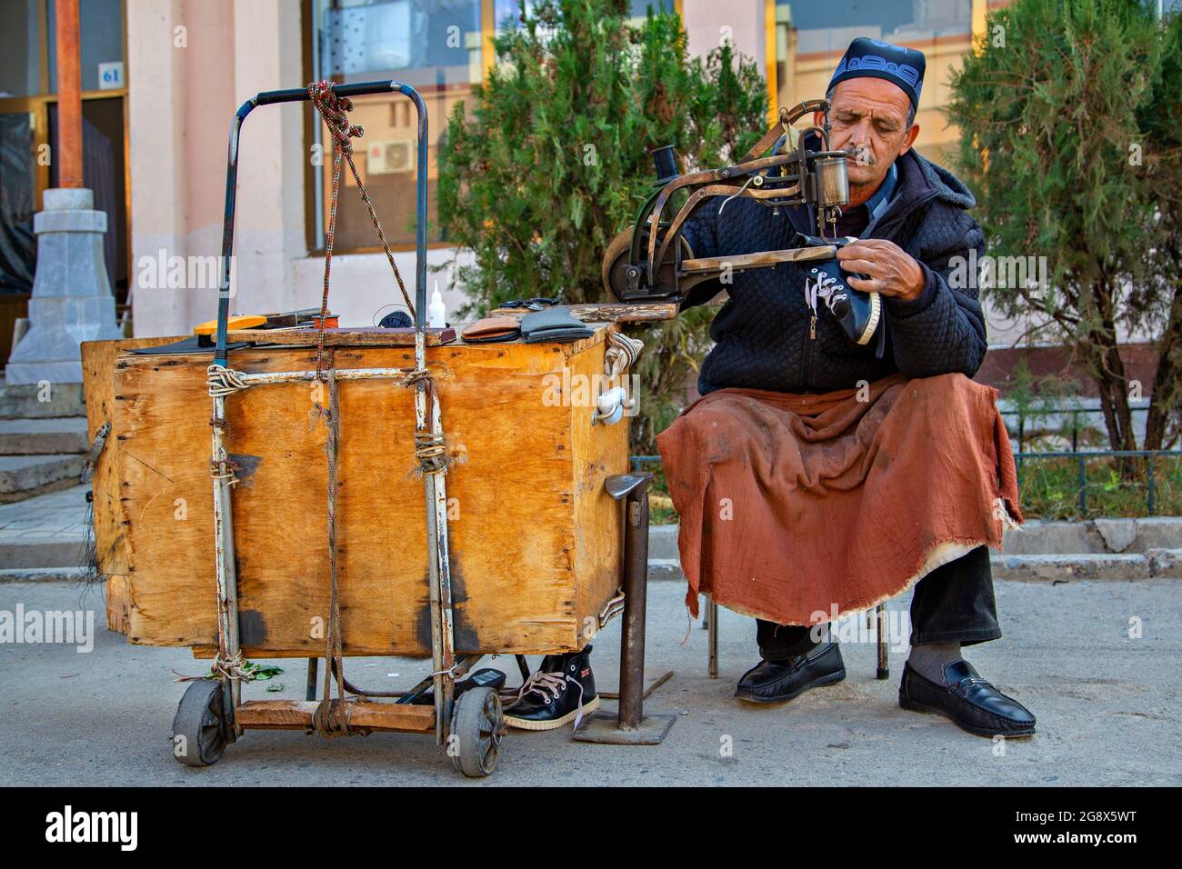 Uomo uzbeko che ripara le scarpe sul suo stand portatile a Samarkand, Uzbekistan Foto Stock
