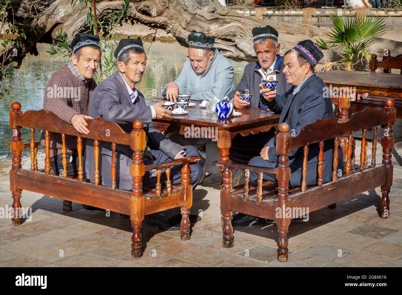 Gruppo di uomini uzbeki che indossano cappelli tradizionali bere tè a Bukhara, Uzbekistan Foto Stock