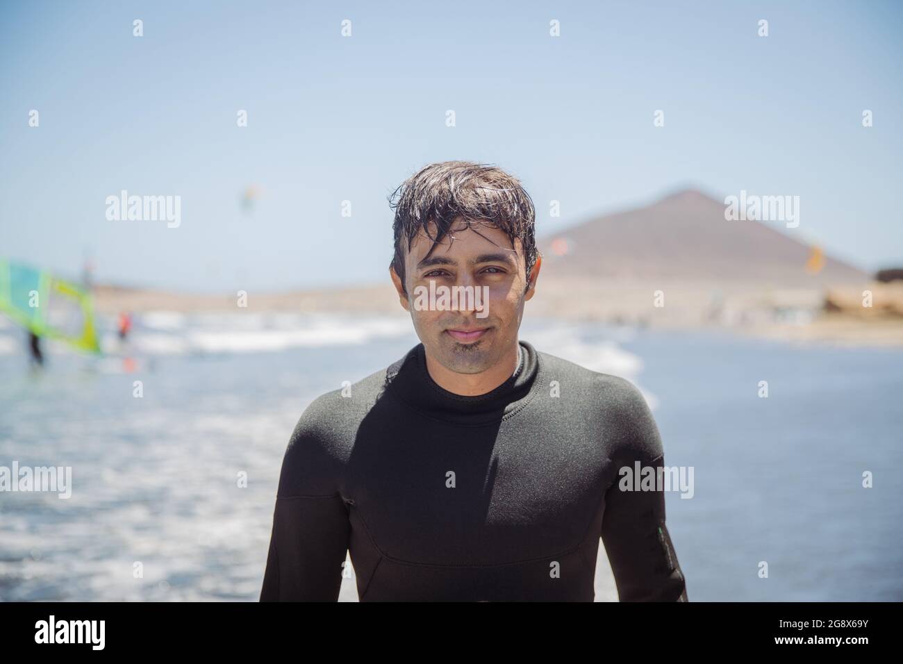 Ritratto di un bell'uomo indiano, surfer alla spiaggia guardando la macchina fotografica, sport estremi e attività di svago - fuoco sul viso Foto Stock