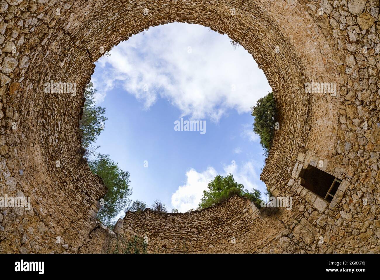 Alte pareti in pietra formano un cerchio perfetto nel cielo. Vecchio pozzo per conservare la neve. Vista ad angolo basso. La Cava de Don Miquel Foto Stock