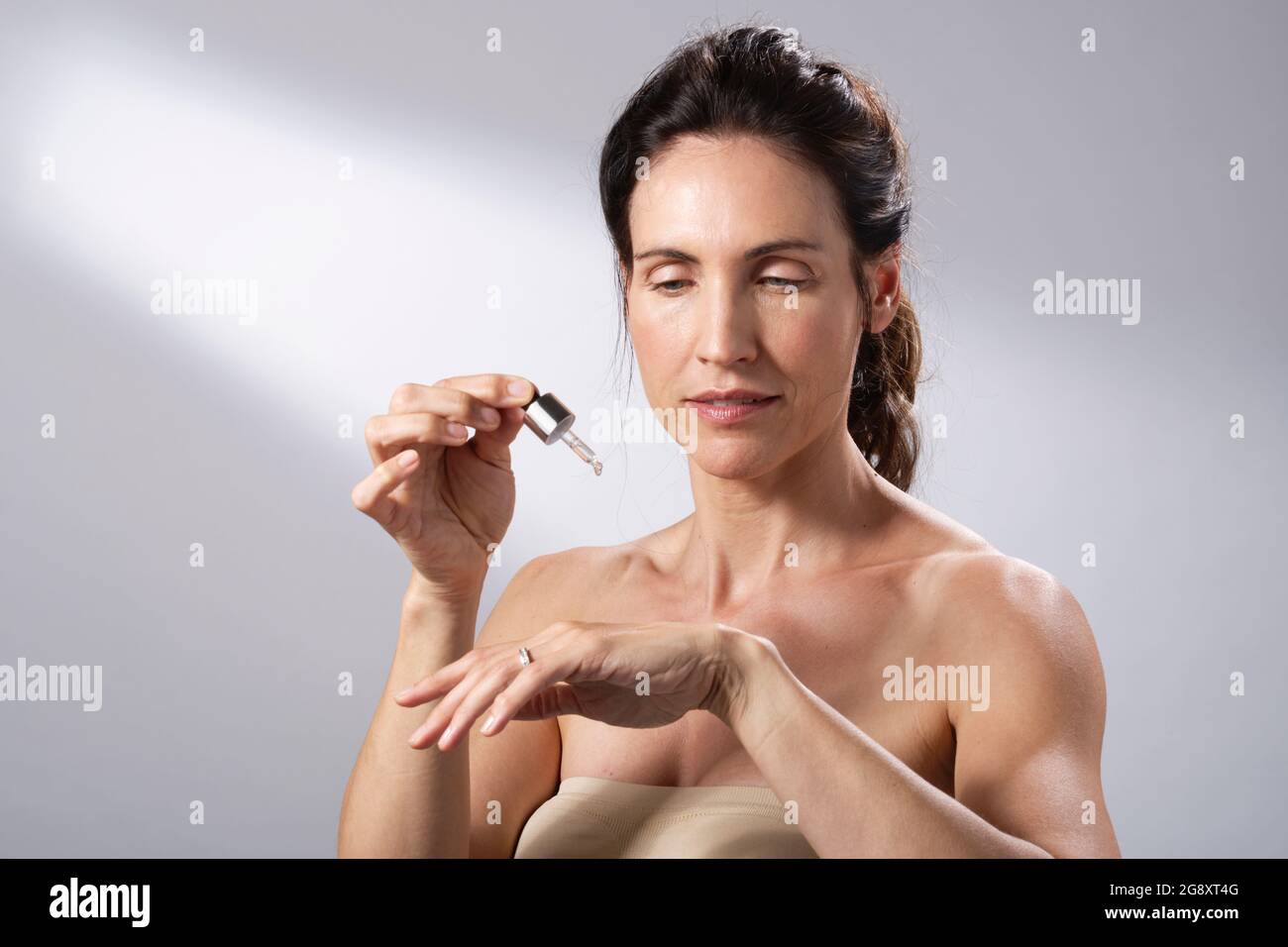 Una giovane donna che usa un contagocce liquido per applicare la pelle alle sue mani. Foto Stock