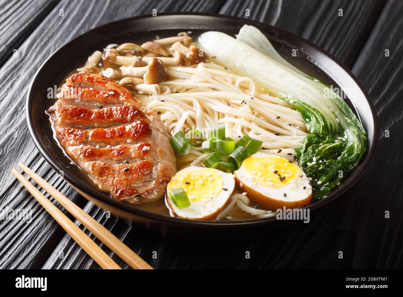 Zuppa asiatica di noodle ramen con anatra, funghi, uova e cavolo pak choi in ciotola su tavolo nero primo piano. Orizzontale Foto Stock