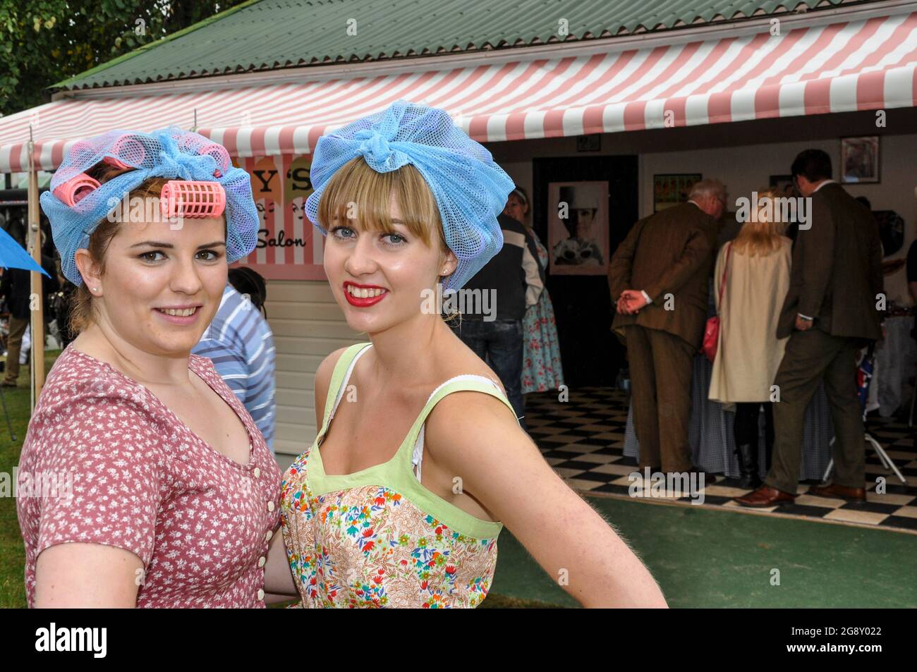 Due donne attraenti al di fuori di un parrucchiere che offre moda retrò ai membri del pubblico al Goodwood Revival, Regno Unito. Ragazze in reti per capelli Foto Stock