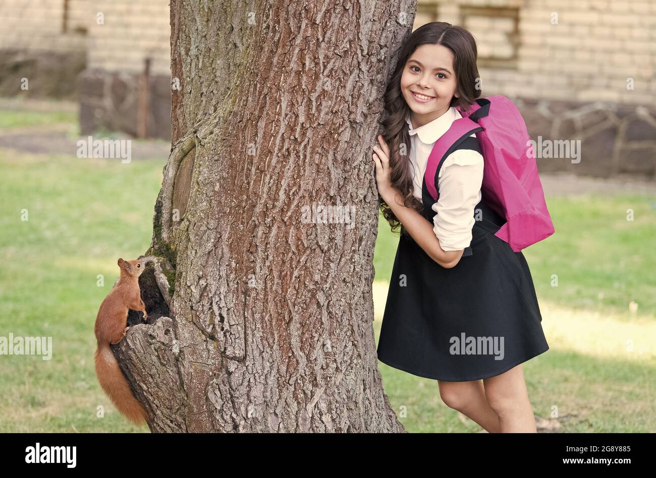 Felice bambino in uniforme con zaino scuola resarch scoiattolo arrampicata albero in parco, zoologia. Foto Stock