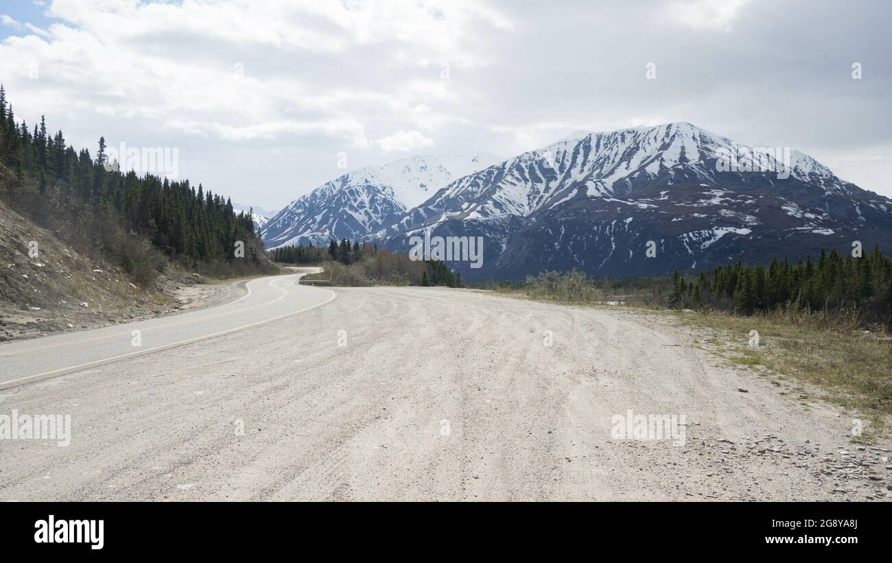 Strada e strada superficie sabbiosa liscia sotto le nuvole - colline innevate sullo sfondo Foto Stock