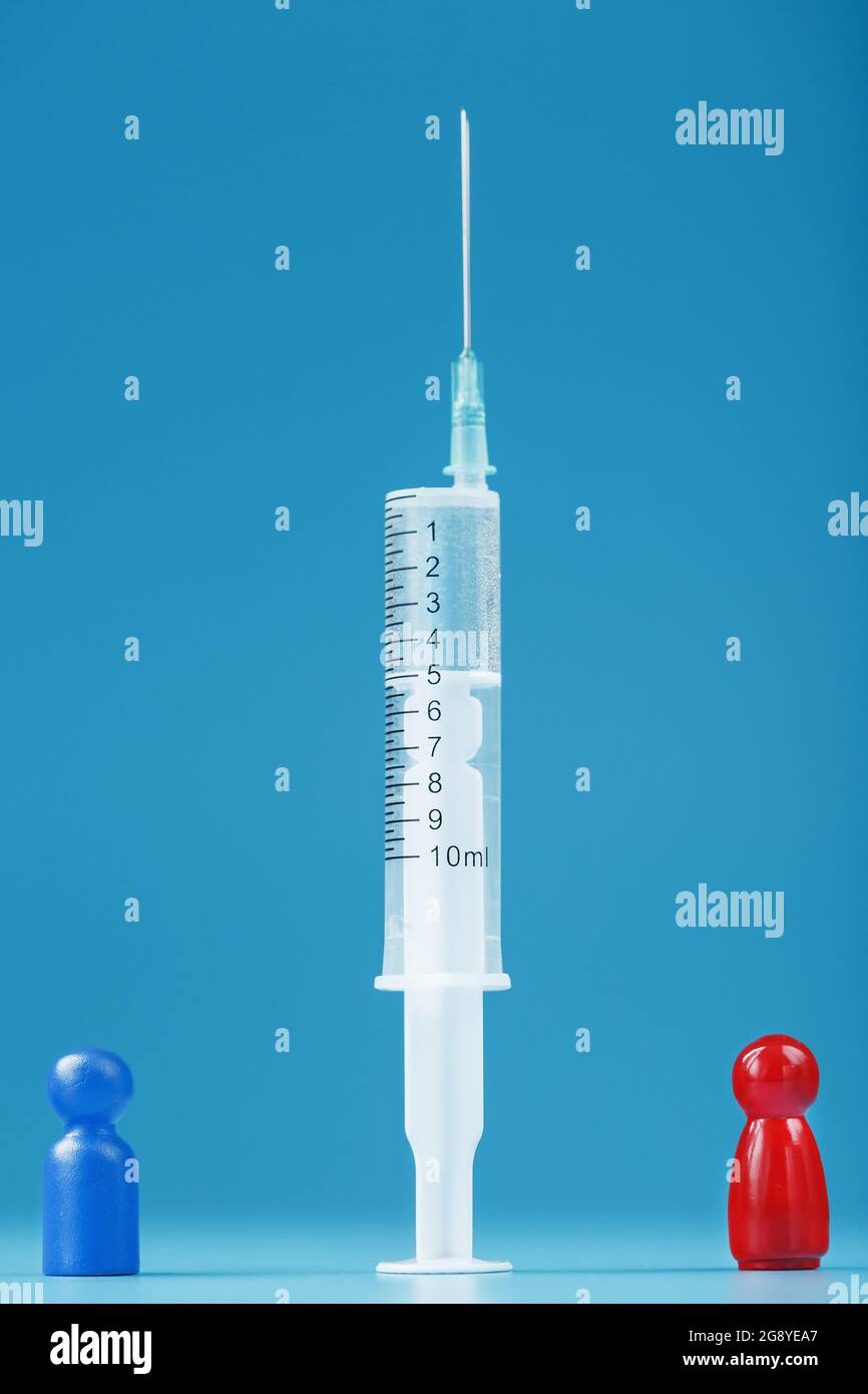 Una miniatura di un uomo blu e rosso tra una siringa con un vaccino. Il concetto di conflitto di vaccinazioni e di vaccinazione. Pro e contro di Foto Stock