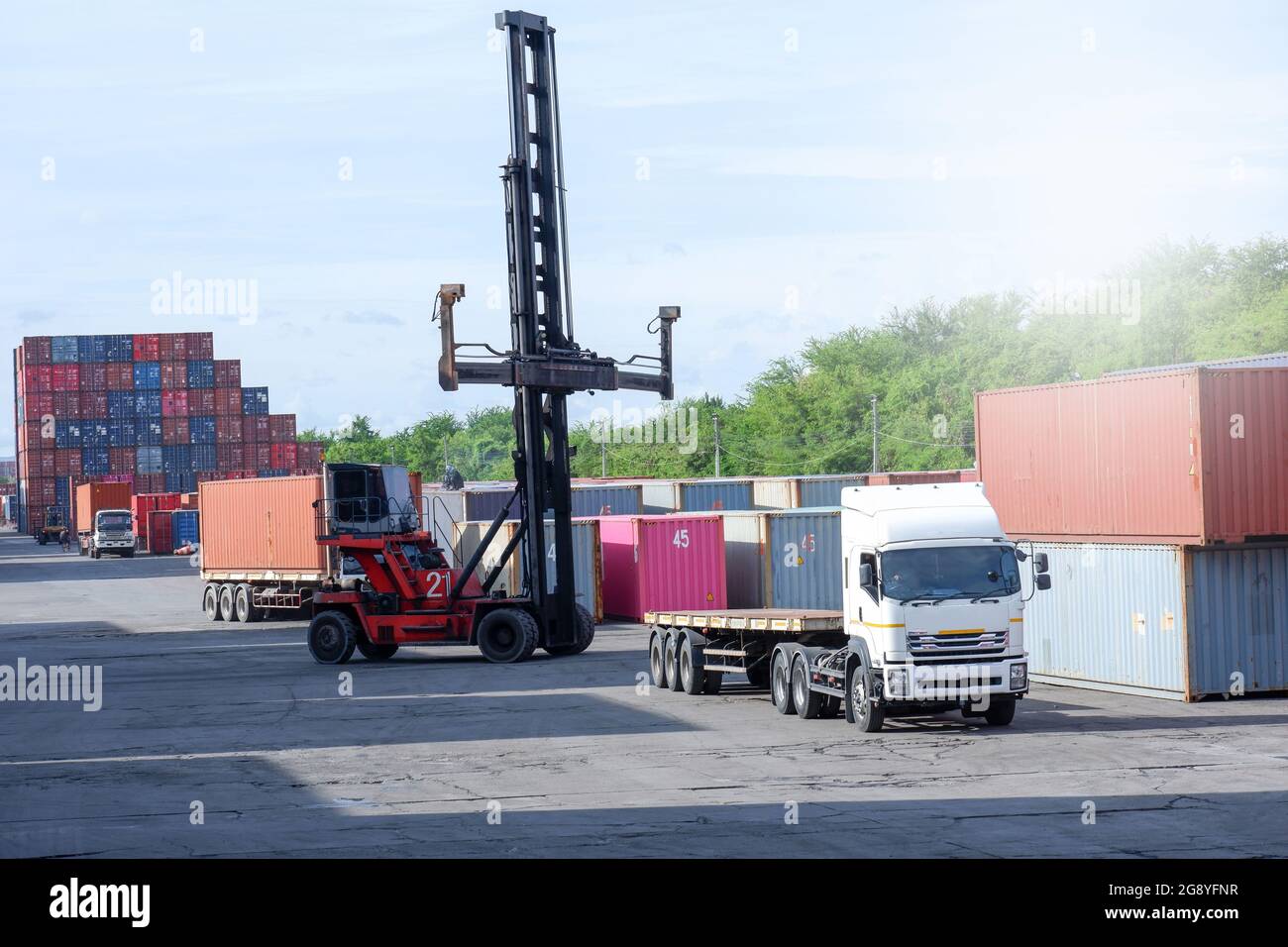 Carrello elevatore a forche di sollevamento del contenitore di carico in cantiere per la spedizione o la dock yard contro Alba cielo con un contenitore di carico in pila in background per i mezzi di trasporto Foto Stock