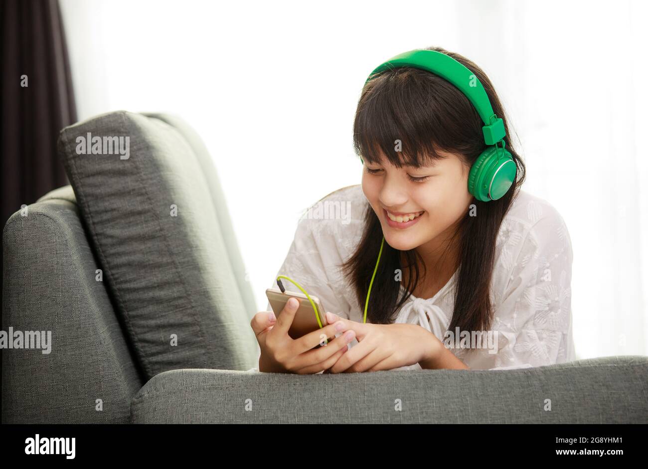 Giovane ragazza asiatica che ascolta la musica con le cuffie e lo smarthphone a casa con la felicità Foto Stock