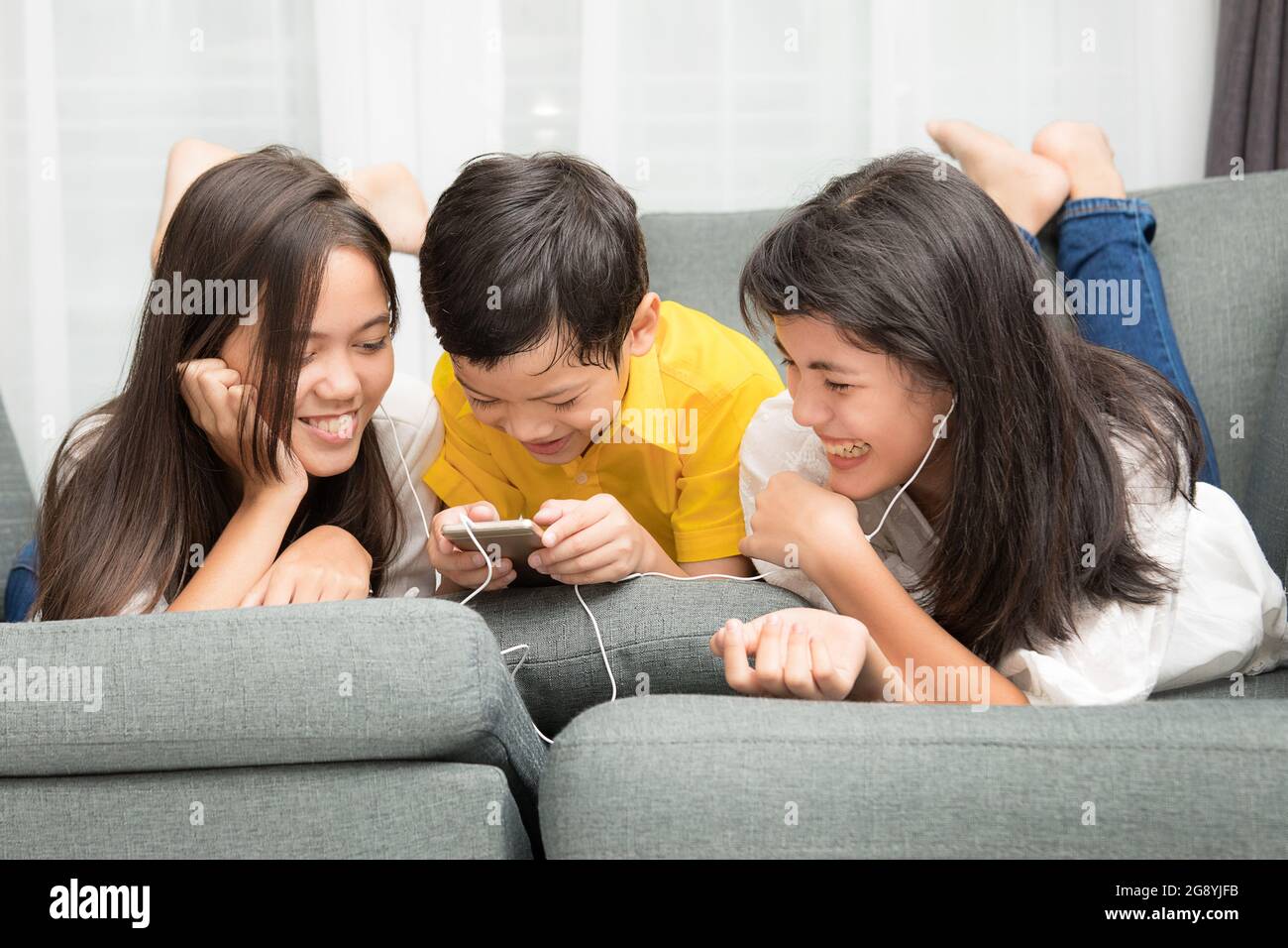 Tre bambini della famiglia asiatica, un ragazzo e due ragazze giocano a casa con la felicità, utilizzando lo smartphone per ascoltare musica e guardare video Foto Stock