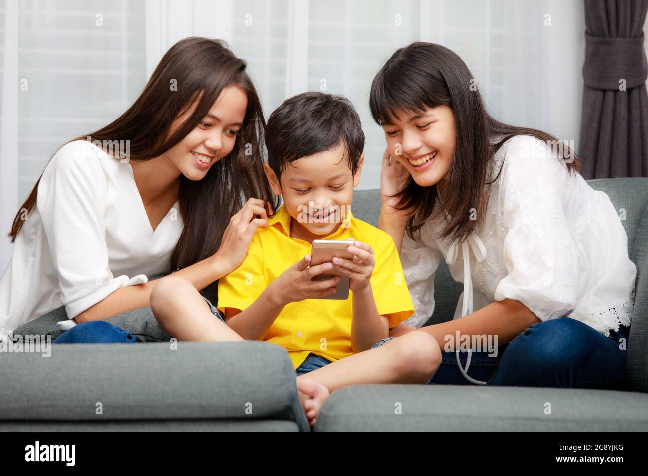 Tre bambini della famiglia asiatica, un ragazzo e due ragazze giocano a casa con la felicità, utilizzando lo smartphone per ascoltare musica e guardare video Foto Stock