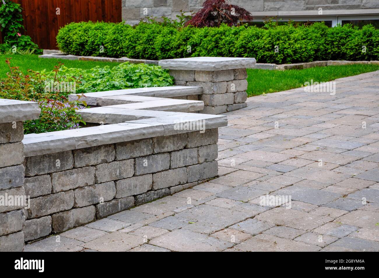 Una parete del sedile con pilastri e rivestimento in pietra naturale contribuisce a definire un vialetto di accesso dell'asfaltatrice in tumbled ed ed è una splendida caratteristica paesaggistica. Foto Stock