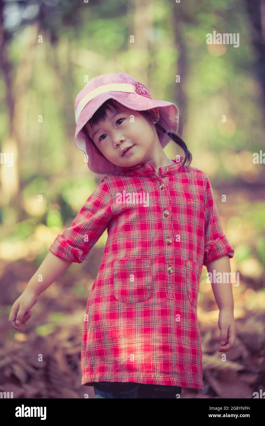 Carino ragazza asiatica poco che gioca su sfondo giardino. Foto in stile retrò. Bambino grazioso in natura. Ritratto esterno. Foto Stock