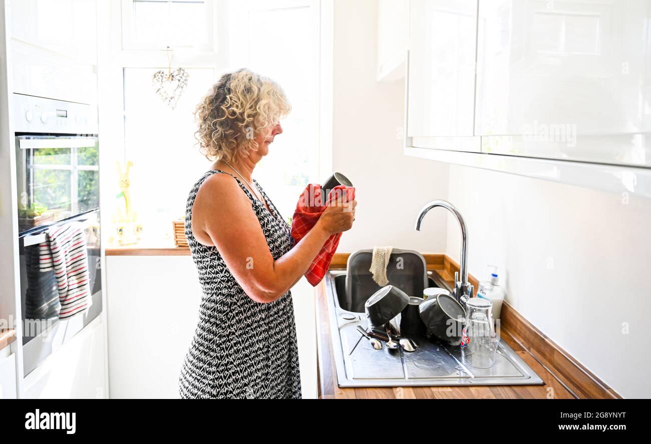 Donna che fa su i piatti in cucina luminosa illuminata nelle faccende domestiche di luce del giorno Foto Stock