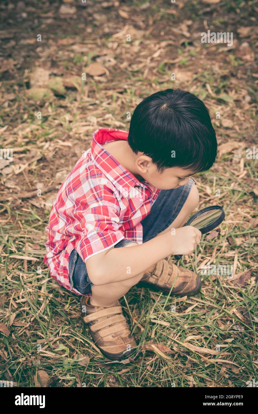 Felice capretto godendosi nella natura. Ragazzo che esplora la natura a terra con una lente d'ingrandimento. All'aperto durante il giorno. Stile vintage. Foto Stock