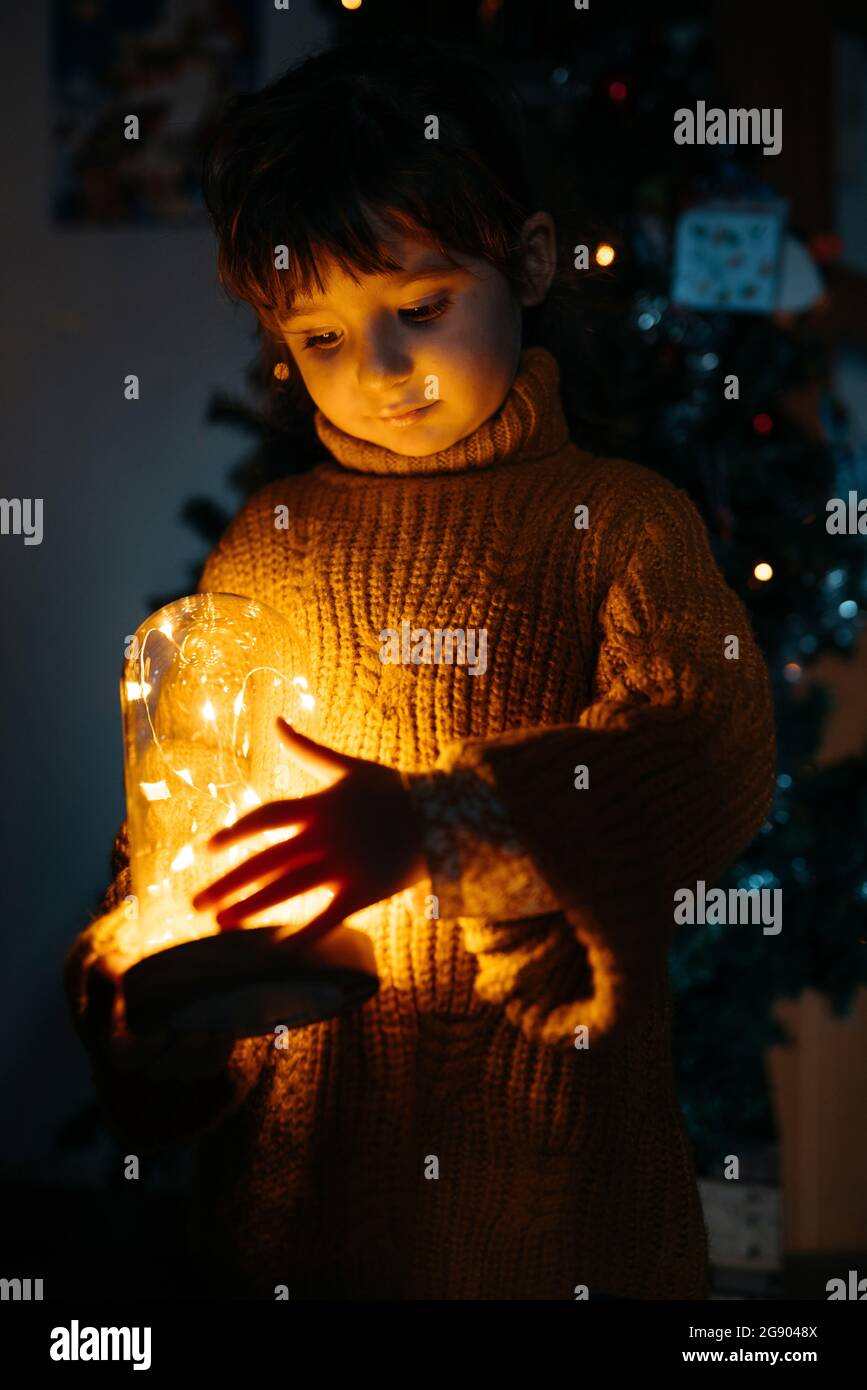 Ragazza carina che guarda le luci gialle incandescenti a casa durante il Natale Foto Stock