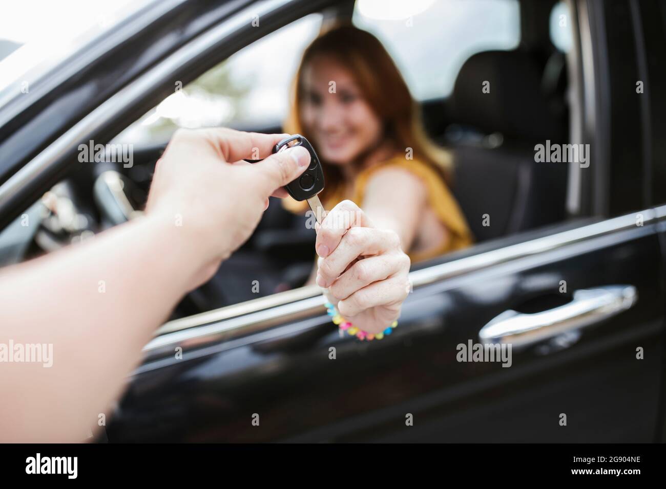 Mano che dà la chiave alla donna seduta in macchina Foto Stock