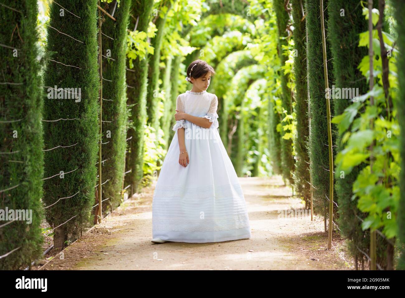 Ragazza in abito bianco comunione guardando giù mentre in piedi in giardino Foto Stock