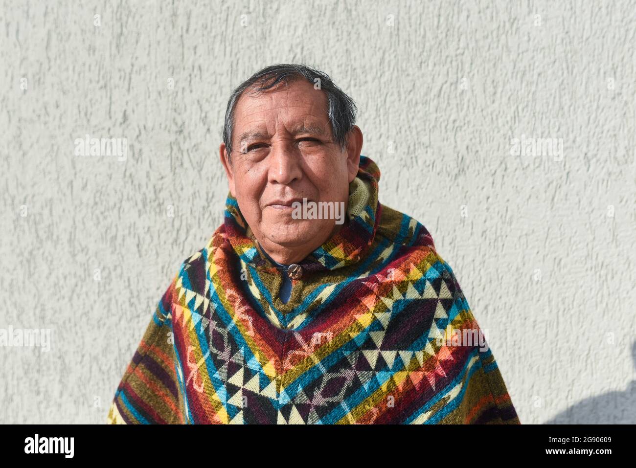 Uomo indigeno senior che indossa poncho di fronte al muro Foto Stock