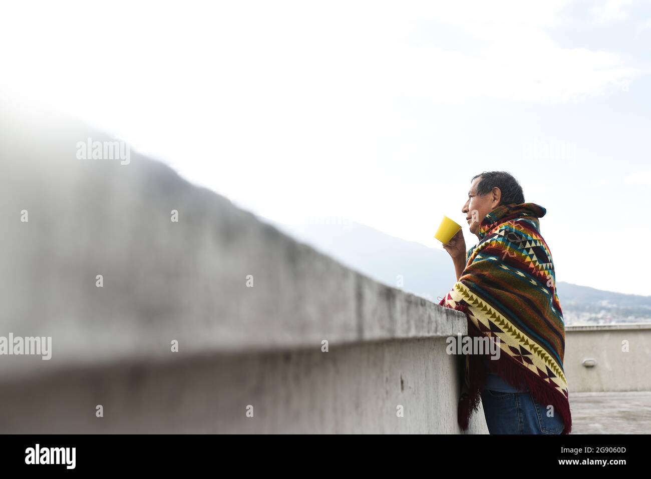 L'uomo indigeno beve caffè mentre si appoggia sulla parete di ritegno sul tetto Foto Stock