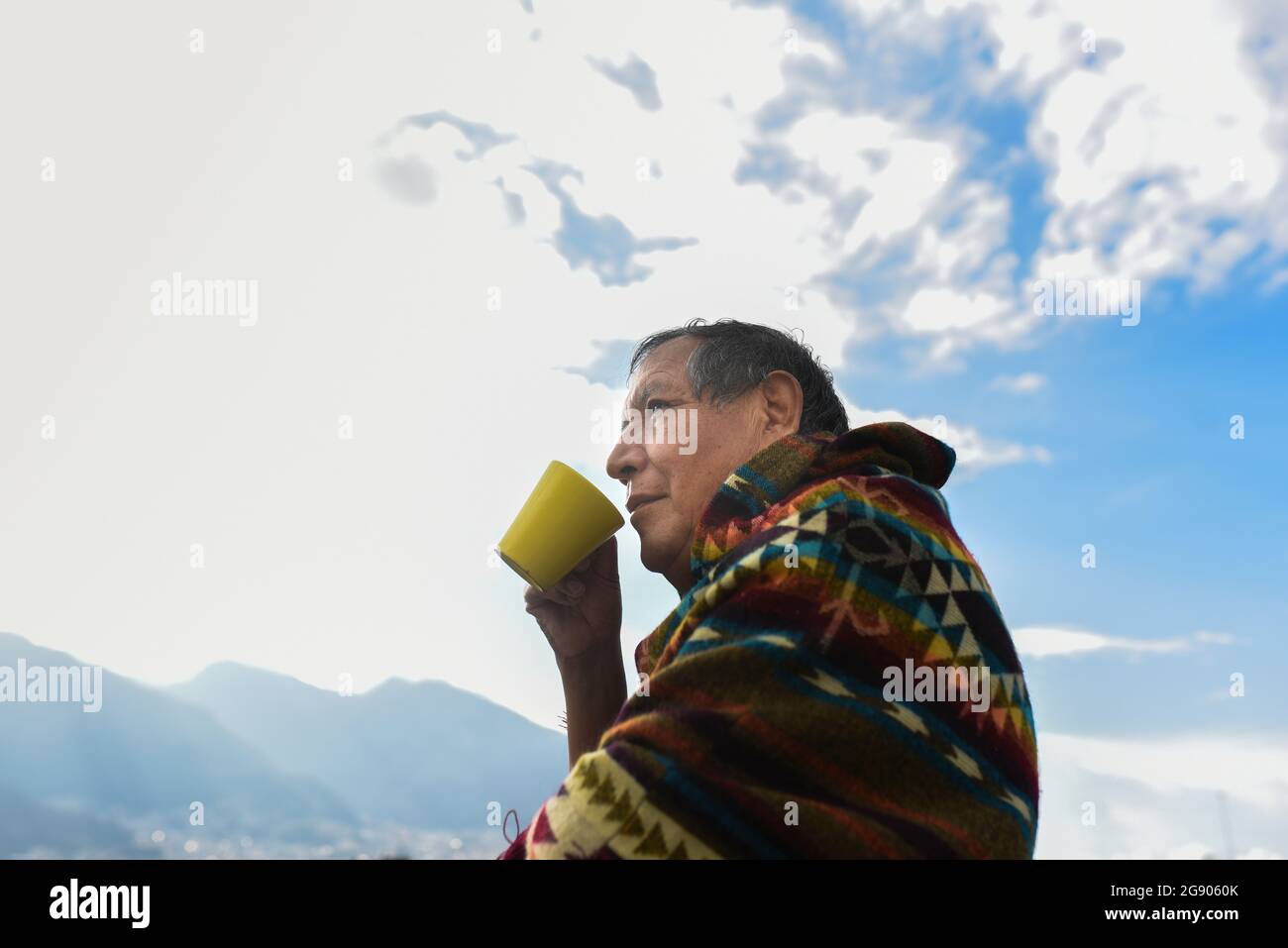 Uomo che indossa il poncho tradizionale guardando lontano mentre beve il caffè Foto Stock