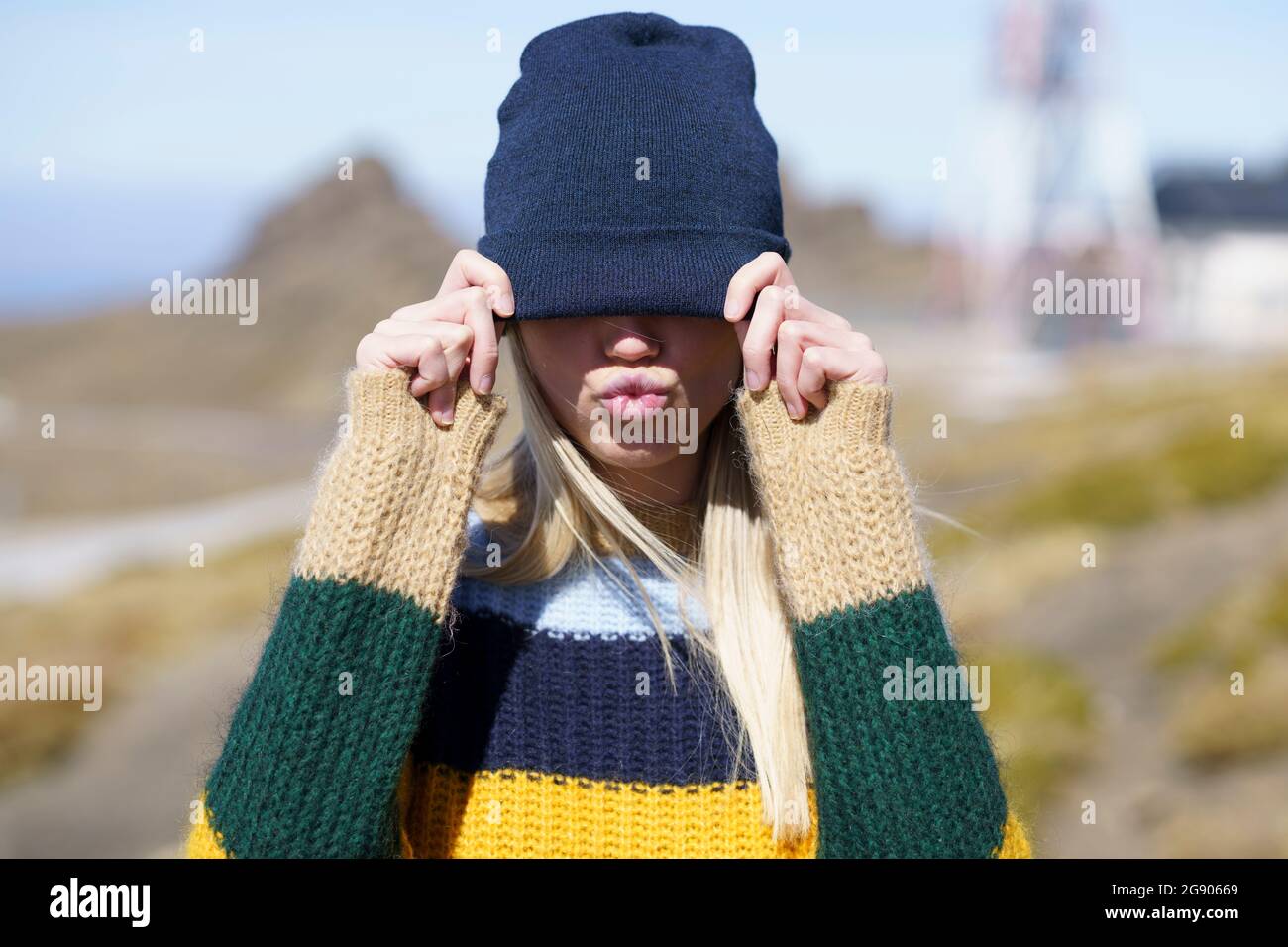 Giovane donna che sbuffa coprendo gli occhi con cappello a maglia Foto Stock