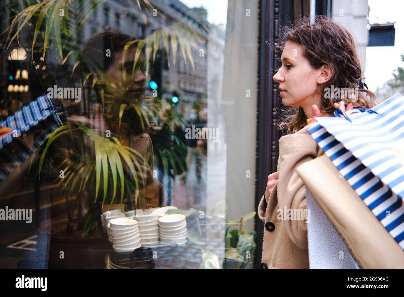 Donna che guarda attraverso la finestra di vetro del negozio mentre trasportano le borse di shopping Foto Stock