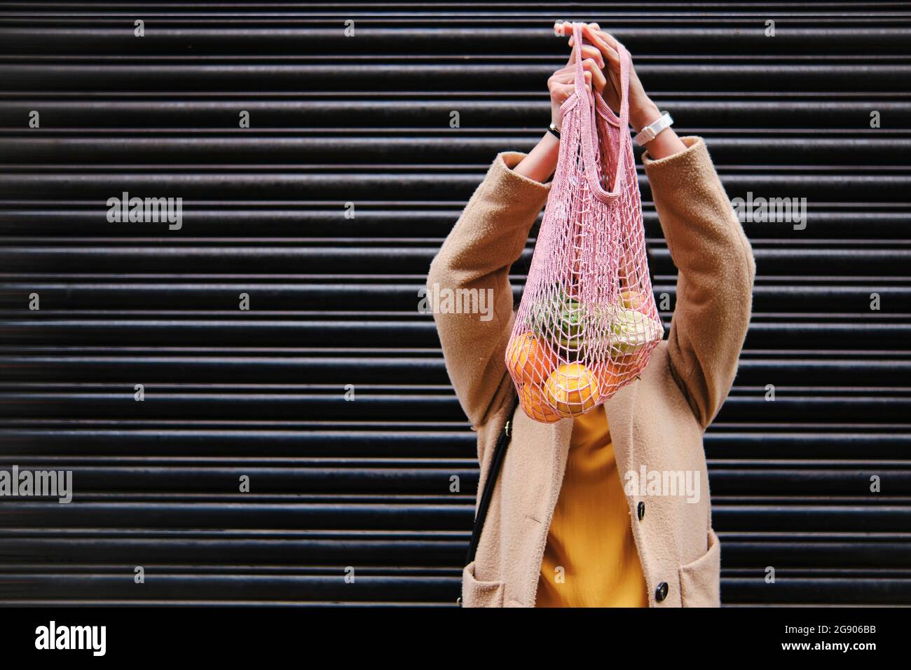 Donna che tiene la borsa in rete vicino alla serranda Foto Stock