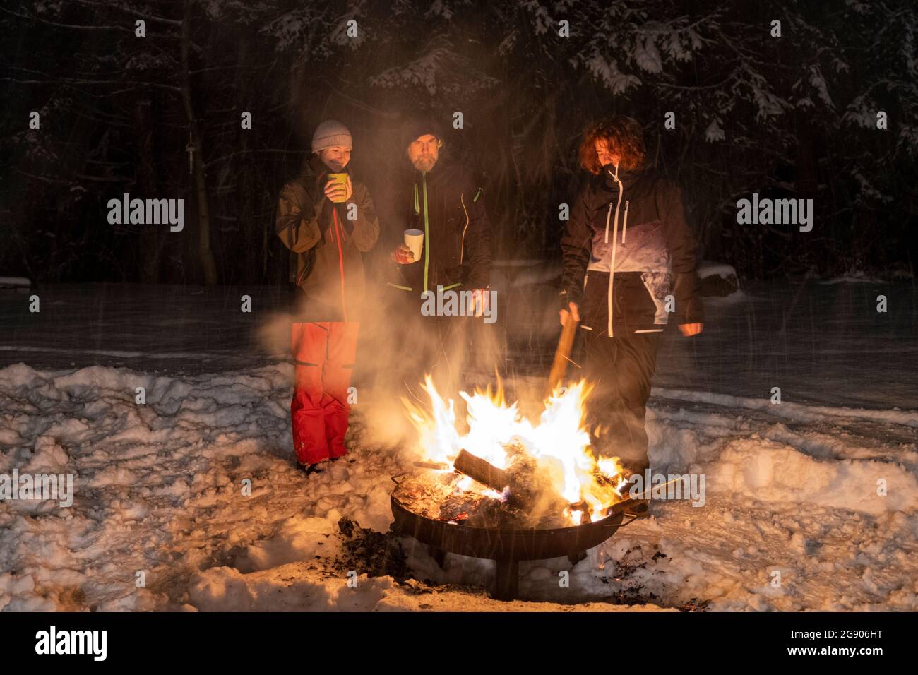 Famiglia in piedi insieme intorno al fuoco durante l'inverno di notte Foto Stock