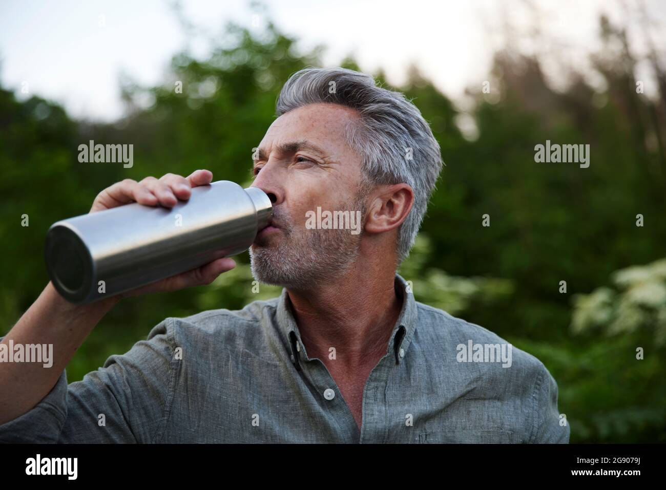 Maschio escursionista bere acqua da bottiglia in foresta Foto Stock