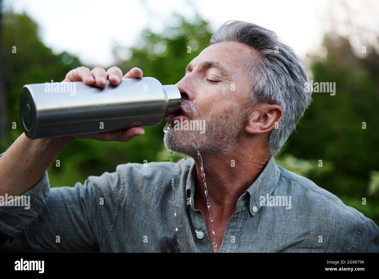 L'uomo assetato che si spillano bevendo acqua dalla bottiglia nella foresta Foto Stock