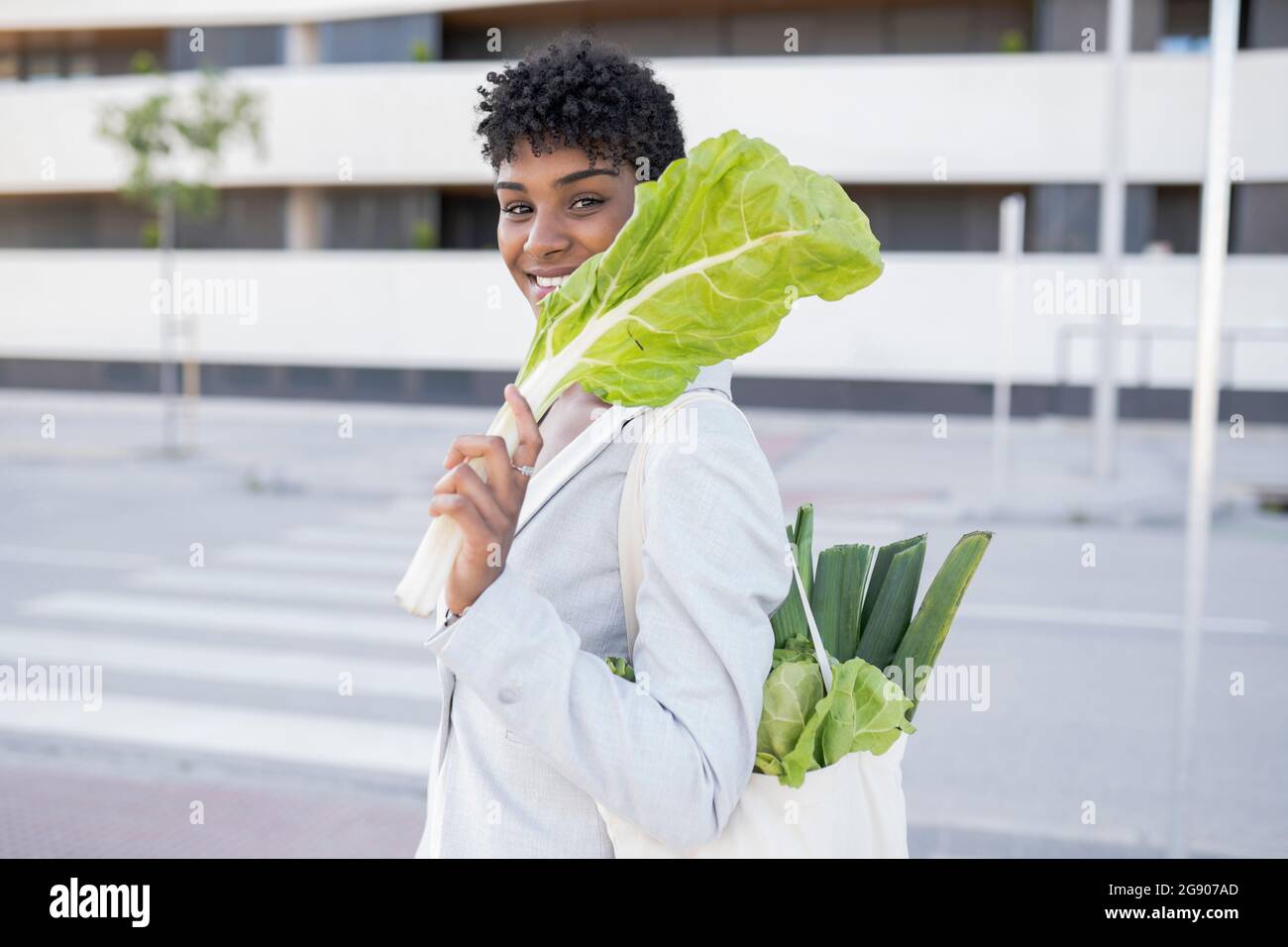 Donna d'affari sorridente che tiene la verdura della foglia in città Foto Stock